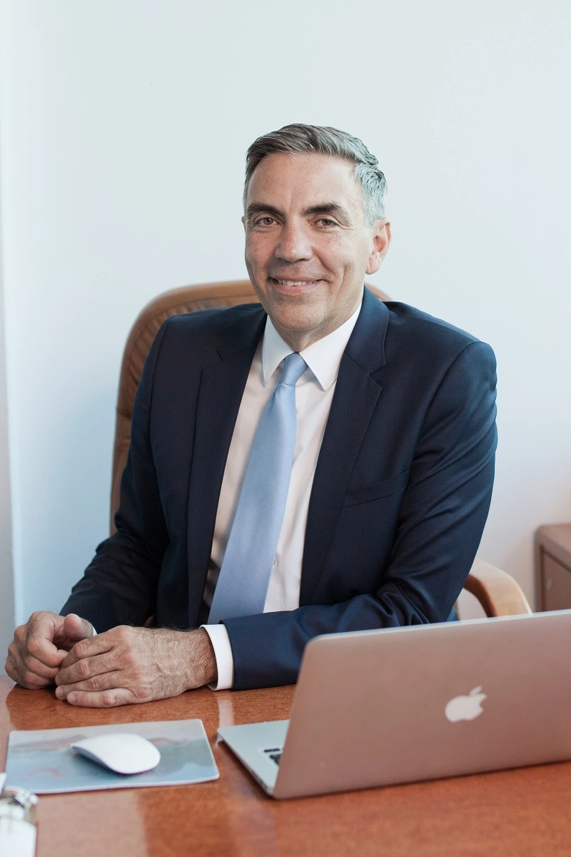 Dragos Anastasiu seated at a desk in a business portrait, wearing a dark suit and light tie.